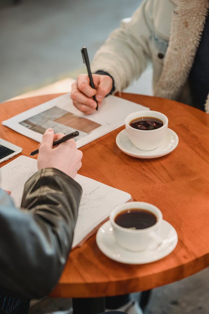 Two people collaborating over documents and coffee in a modern café setting.